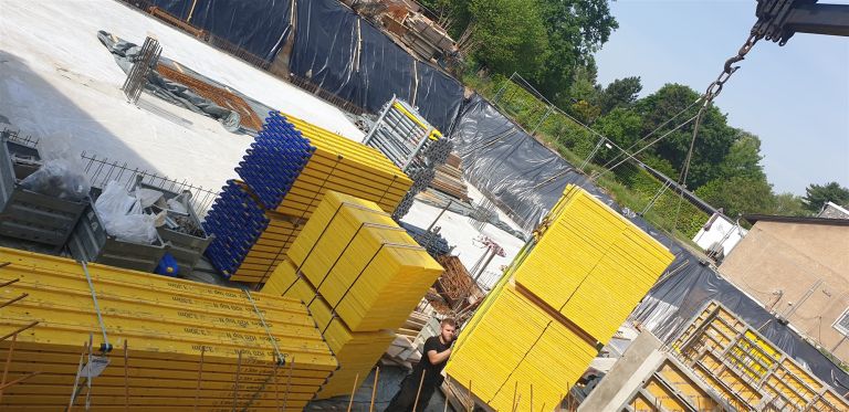 Gestapelte gelbe Schalungselemente und blaue Deckenstützen auf einer Baustelle