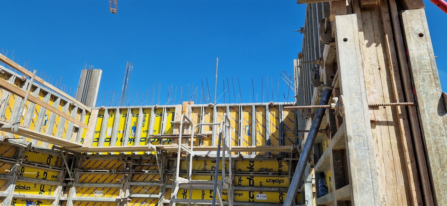 Gelbe Rahmenschalung auf einer Rohbaustelle, dahinter der bereits betonierte Baukörper vor blauem Himmel